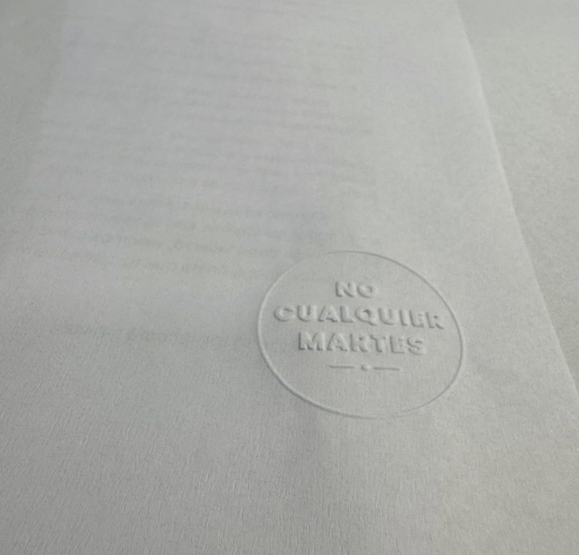 Sello de agua de No Cualquier Martes en relieve sobre papel, con luz rasante.